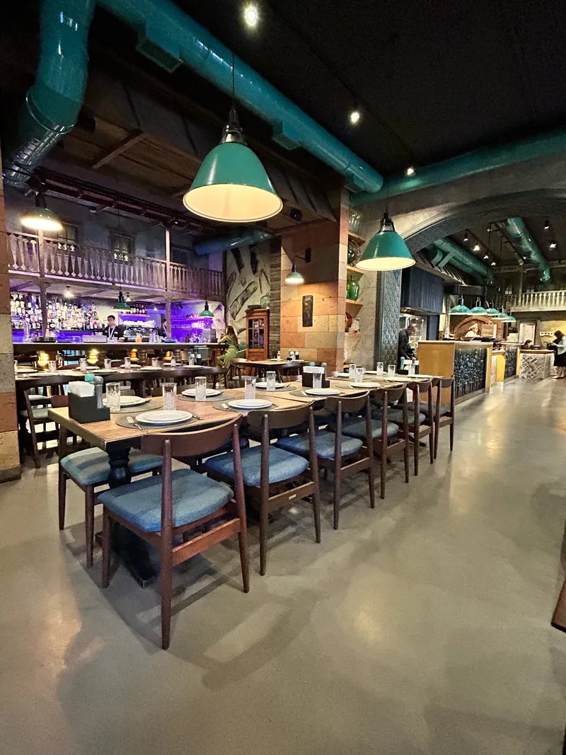 The hall: long tables with blue chairs under teal pendant lamps and teal air ducts, the bar at the back